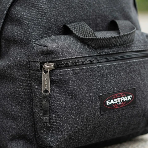 Close-up of a charcoal speckled Eastpak backpack front pocket with the red logo patch and metal zipper pull